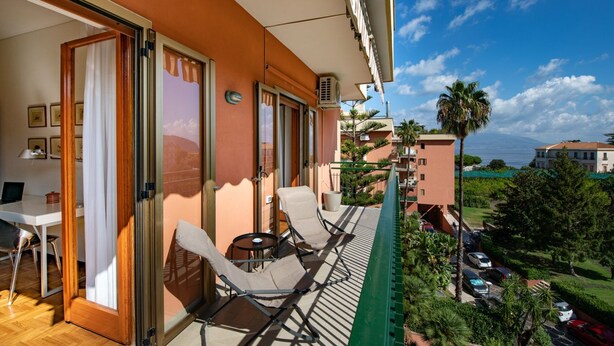 Un balcón con dos sillones de relax y una mesita, con vista a una zona costera con palmeras y coches aparcados.