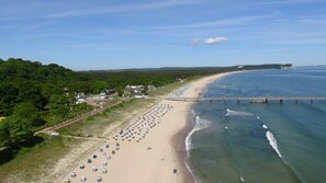 A beach with rows of beach umbrellas and a pier extending into the water. - Terrace, free use of the AHOI adventure pool and sauna - Apartment with Ocean View 77 - (Göhren)