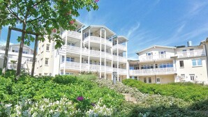 A multi-story hotel with balconies, surrounded by greenery and white flowers. - Terrace, free use of the AHOI adventure pool and sauna - Sea view apartment 77 - (Göhren)