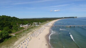 A beach with rows of beach umbrellas and a pier extending into the water. - Terrace, free use of the AHOI adventure pool and sauna - Sea view apartment 77 - (Göhren)