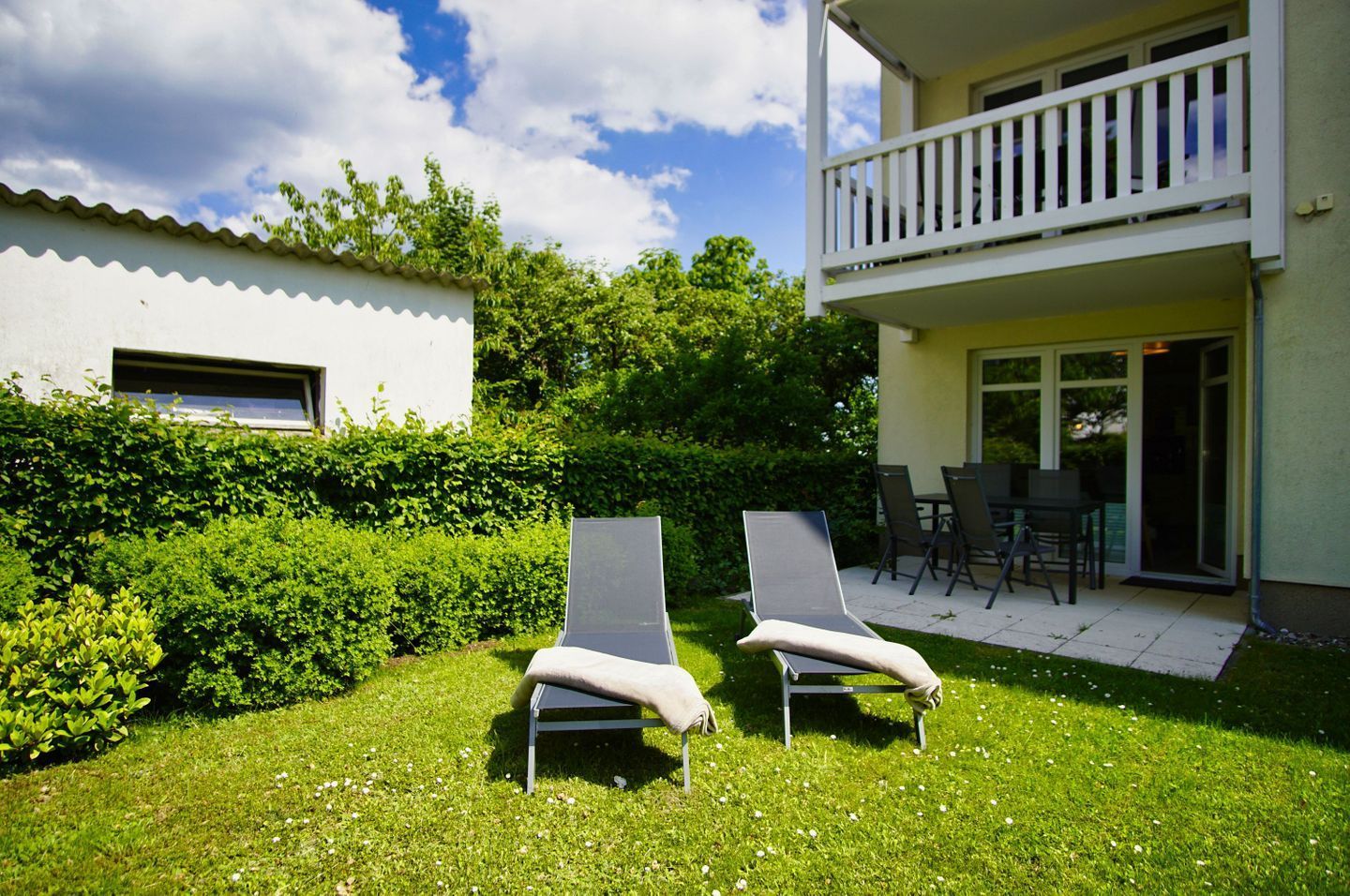 Un patio trasero con dos sillones, una mesa de patio y sillas, rodeado de setos bien cuidados.