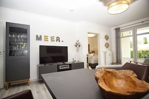 A modern living room with a flat-screen TV, a dining table, and a built-in wine rack.