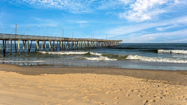 Una playa con un muelle de madera que se adentra en el océano.