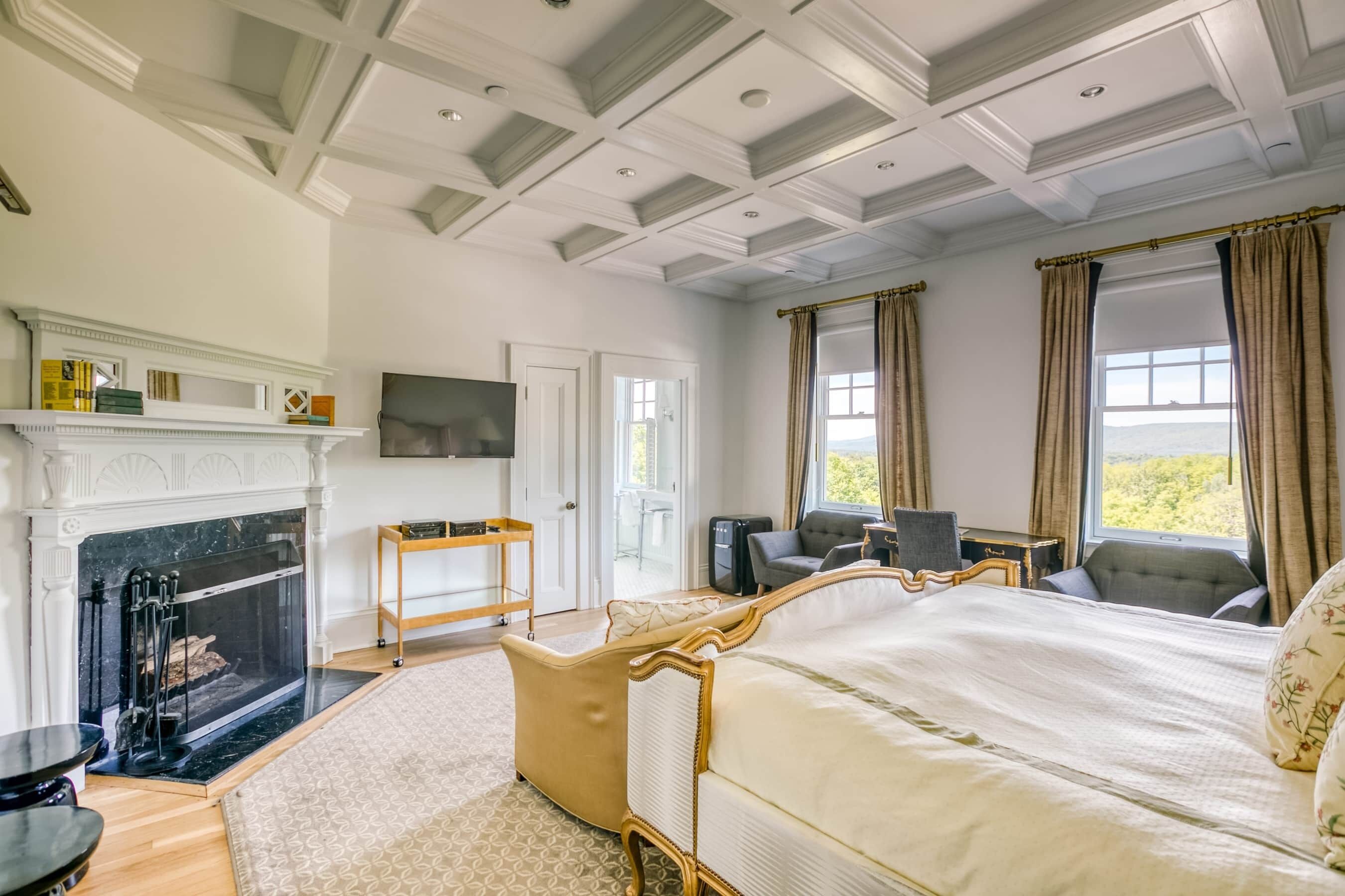 A spacious bedroom with a large bed, a fireplace, a television, and a view of the outdoors.