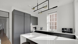 Een moderne keuken met een groot eiland, een inbouwoven en een raam met uitzicht op een bakstenen muur.