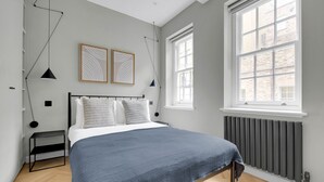 Een moderne slaapkamer met een bed, twee nachtkastjes, een radiator en grote ramen.