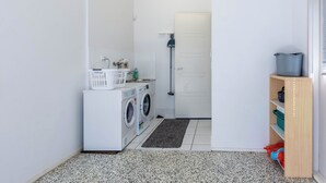 Een wasserette met een wasmachine, droger en een klein plankje met wasmanden.