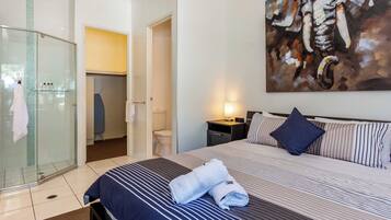 Une chambre d’hôtel avec un lit, une douche en verre, un tableau au mur et une table de chevet avec une lampe.