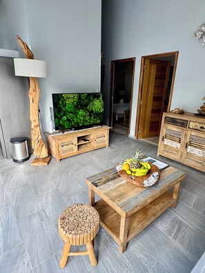 Un salon moderne doté d’un téléviseur à écran plat, de meubles en bois, d’un panier de fruits posé sur une table basse et d’un tabouret en bois original.