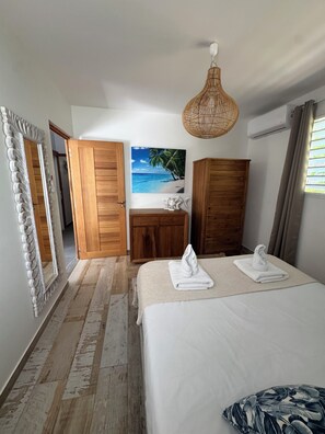 A hotel room with a bed, a wooden wardrobe, a dresser, a mirror, and a painting of a beach scene.