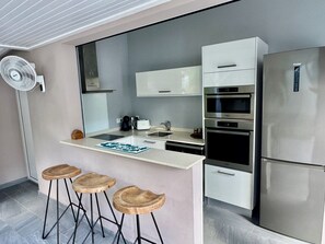 Une cuisine moderne dotée d’un îlot central intégré, d’appareils électroménagers en acier inoxydable et d’un grand miroir au-dessus du plan de travail.