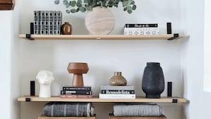 Habitación minimalista con dos taburetes de madera, una planta en maceta y libros en estanterías.