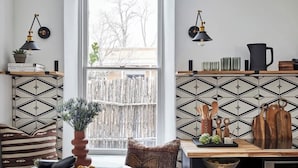 Una cocina con un salpicadero blanco y negro de diseño geométrico, una mesa de madera con un cuenco de fruta, un florero con plantas verdes y un refrigerador negro.