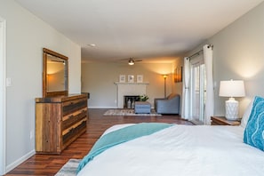 A bedroom with a bed, dresser, chair, fireplace, and a view of the outdoors.