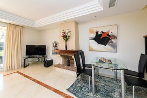 A modern living room with a flat-screen TV, a glass dining table, black chairs, a fireplace, and a large abstract painting on the wall. - VILLA RIVIERA - Luxury villa with private pool in a fabulous urbanization on the Costa del (Mijas)