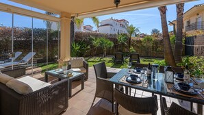 A patio with wicker furniture, a glass-top table, and a view of a white building and palm trees. - VILLA RIVIERA - Luxury villa with private pool in a fabulous urbanization on the Costa del (Mijas)