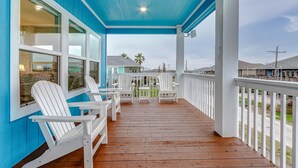 A covered porch with white Adirondack chairs and a wooden deck. - Amazing Outdoor Space, Beautiful Interior with King Beds, Easy Walk to Beach! (Crystal Beach)