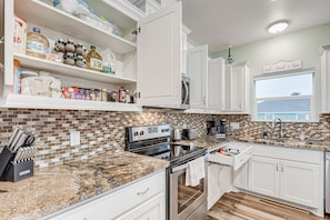 A modern kitchen with white cabinetry, granite countertops, and a backsplash of brown and beige tiles.
