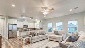 A spacious living area with a kitchen, a ceiling fan, and large windows. - Amazing Outdoor Space, Beautiful Interior with King Beds, Easy Walk to Beach! (Crystal Beach)
