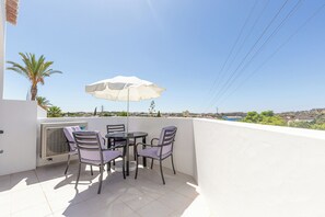 Uma varanda com mesa, cadeiras, guarda-sol e vista para a paisagem.