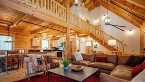 Ein geräumiger Wohnbereich mit hohen Decken, Holzbalken, einer Treppe und einer Küche im Hintergrund.