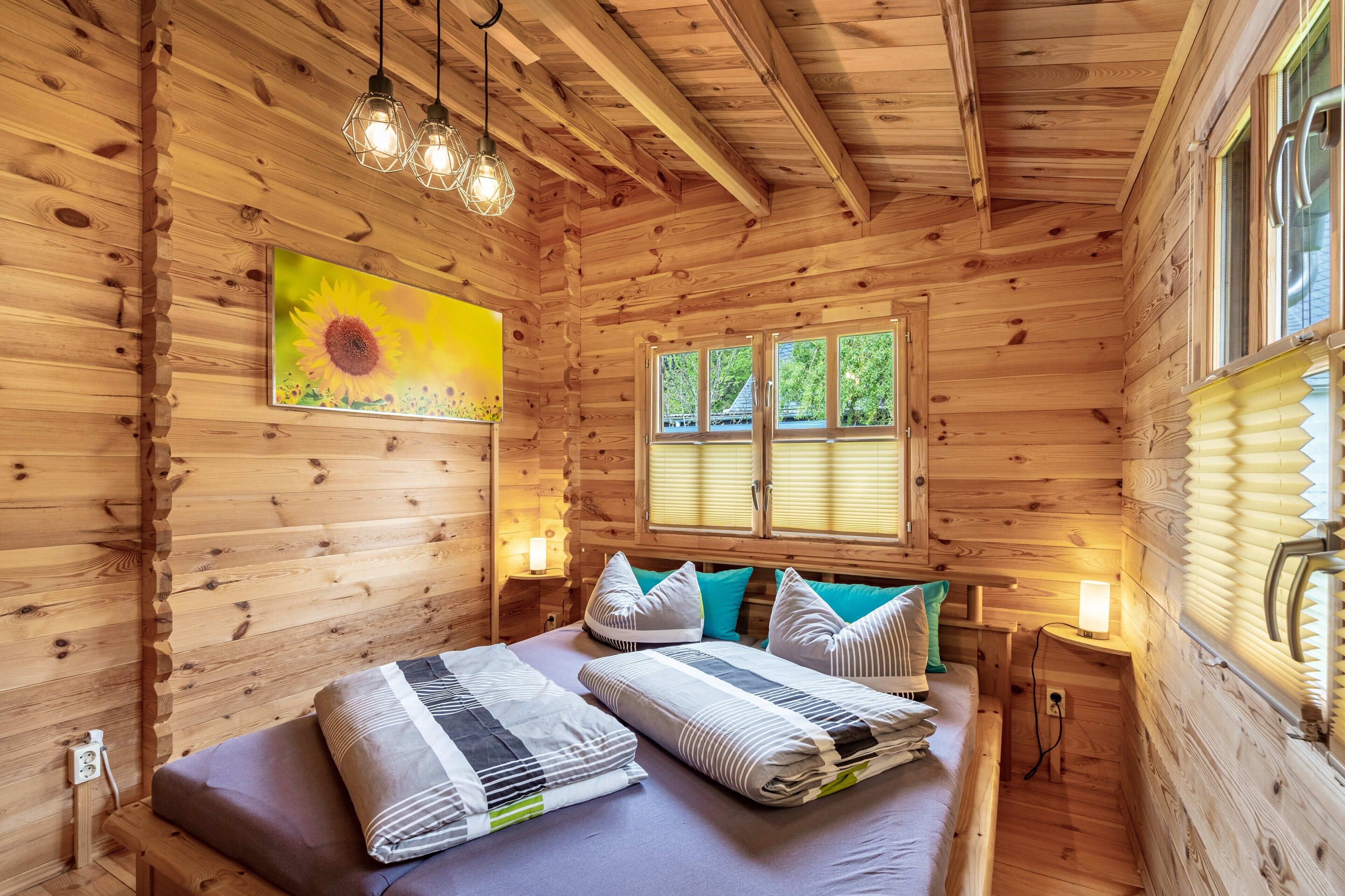 A wooden cabin bedroom with a bed, pillows, a painting, and a window.