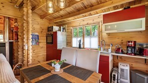 Ein Holzblockhaus-Interieur mit einem Esstisch, Stühlen, einer Küchenzeile inklusive Mikrowelle und einem Fenster.