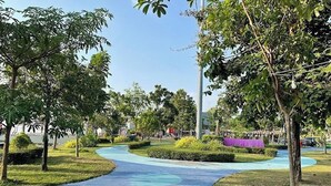 A pathway in a park with trees and a purple structure in the background.