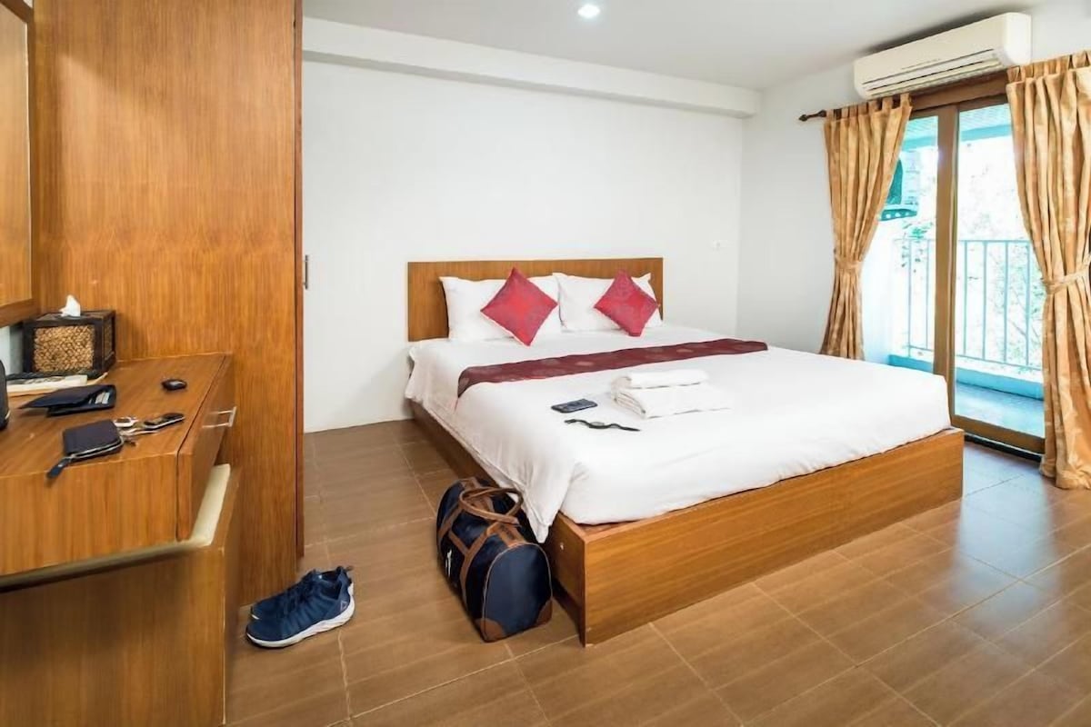A hotel room with a wooden bed, a desk with a computer, and a suitcase on the floor.