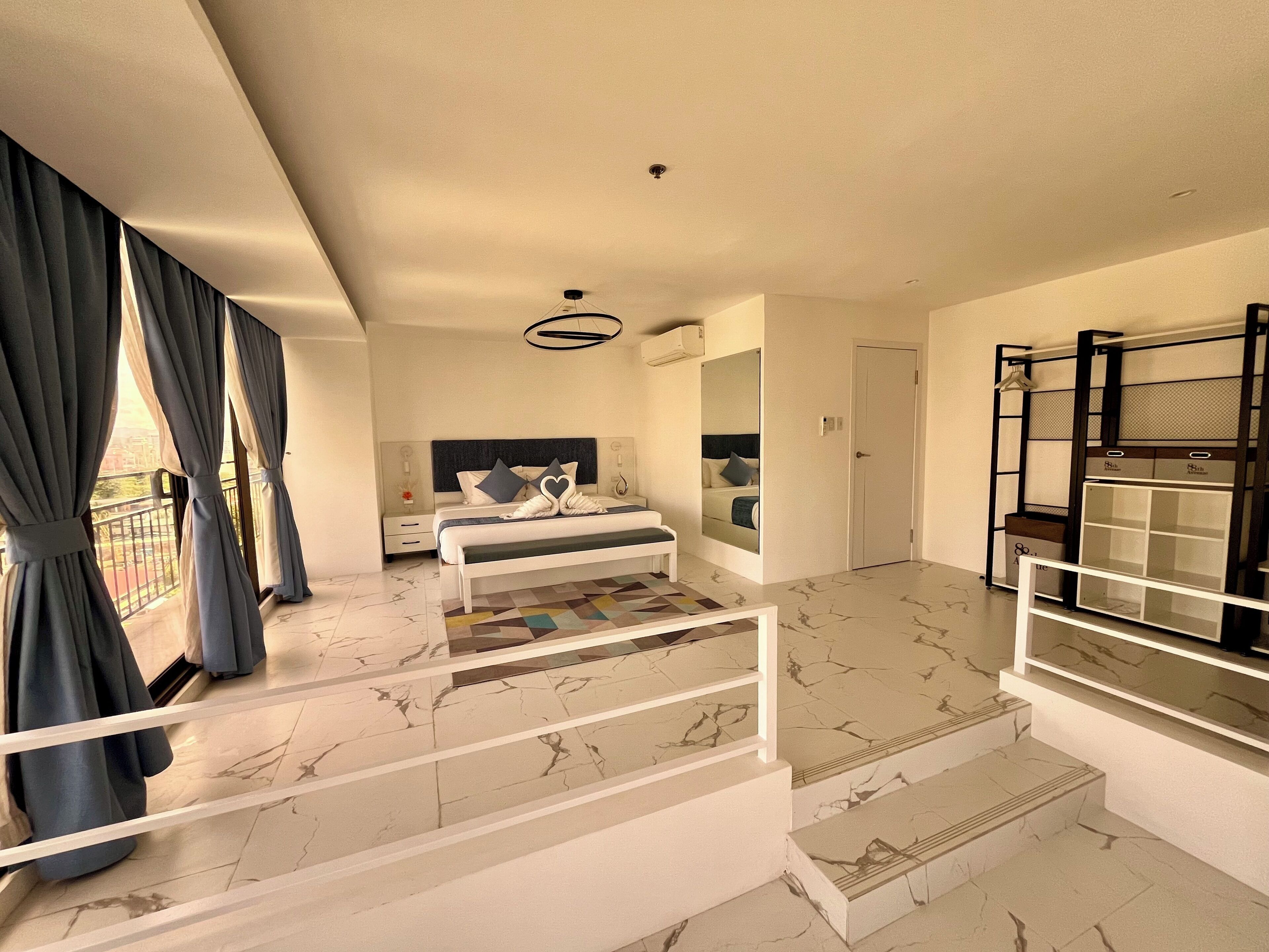 A modern bedroom with a bed, bedside tables, a large mirror, and a staircase leading to an upper level.