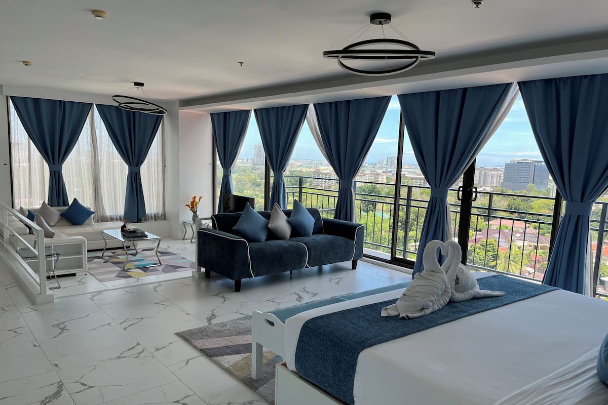 Een moderne hotelkamer met een groot bed, een bank, een salontafel en een balkon met uitzicht over de stad.