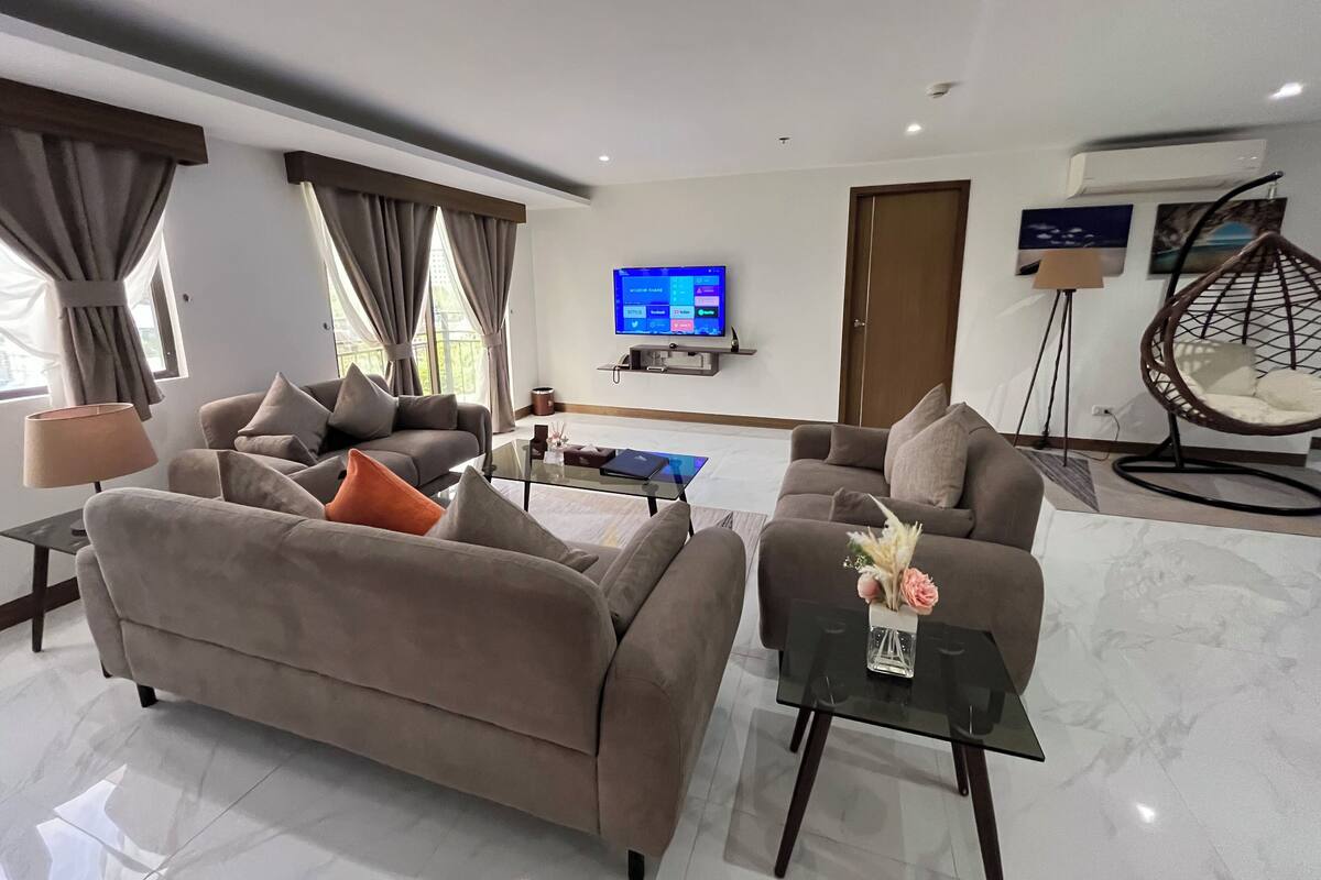 Een moderne woonkamer met twee banken, een glazen salontafel, een hangstoel en een flatscreen televisie aan de muur.