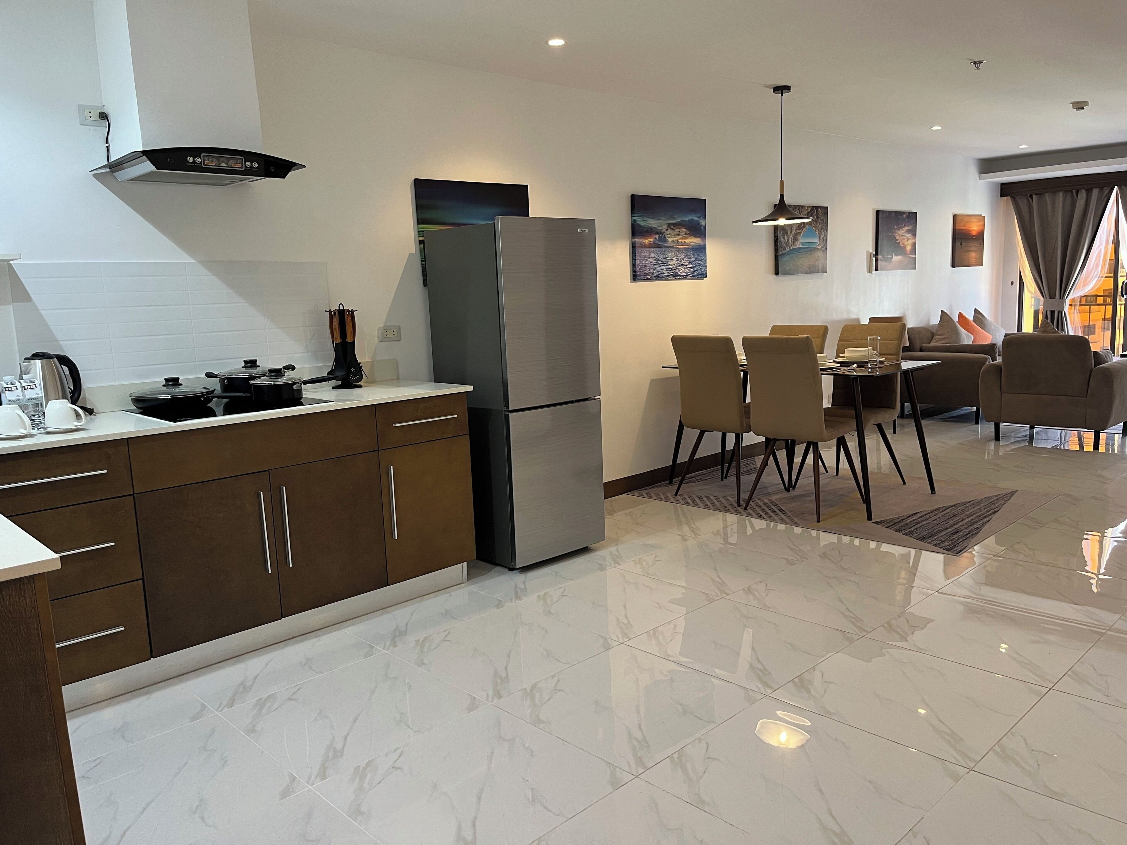 A modern kitchen with a stainless steel refrigerator, a dining area with a table and chairs, and a living area with a sofa and a view of the outdoors.