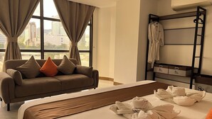A hotel room with a bed, a sofa, a window with curtains, a rack with robes, and storage boxes. - 88th Avenue (Cebu City)