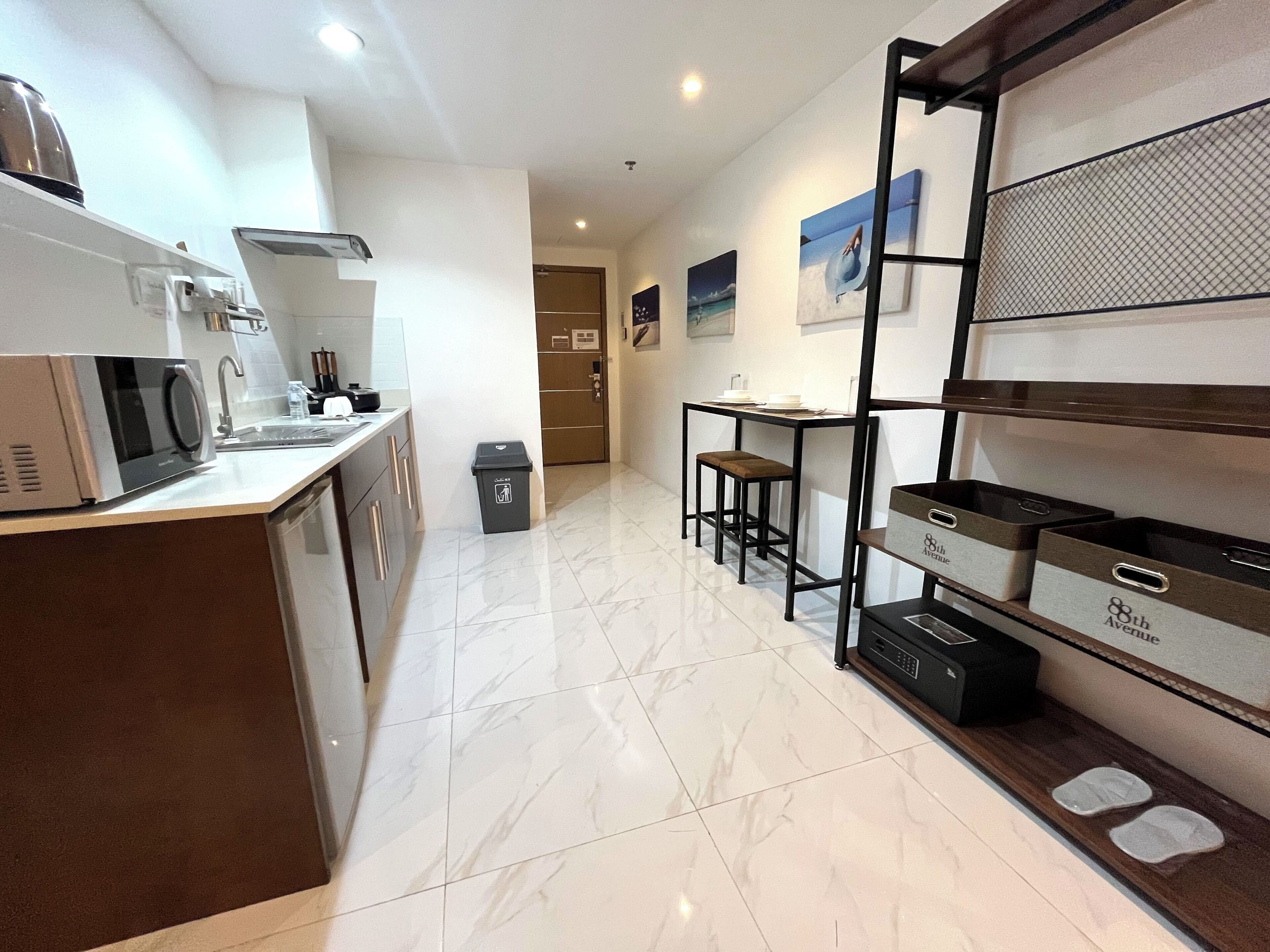A modern kitchen with a microwave, sink, and a small trash bin. There is a dining area with a table and chairs, and a wall-mounted shelf with storage boxes.