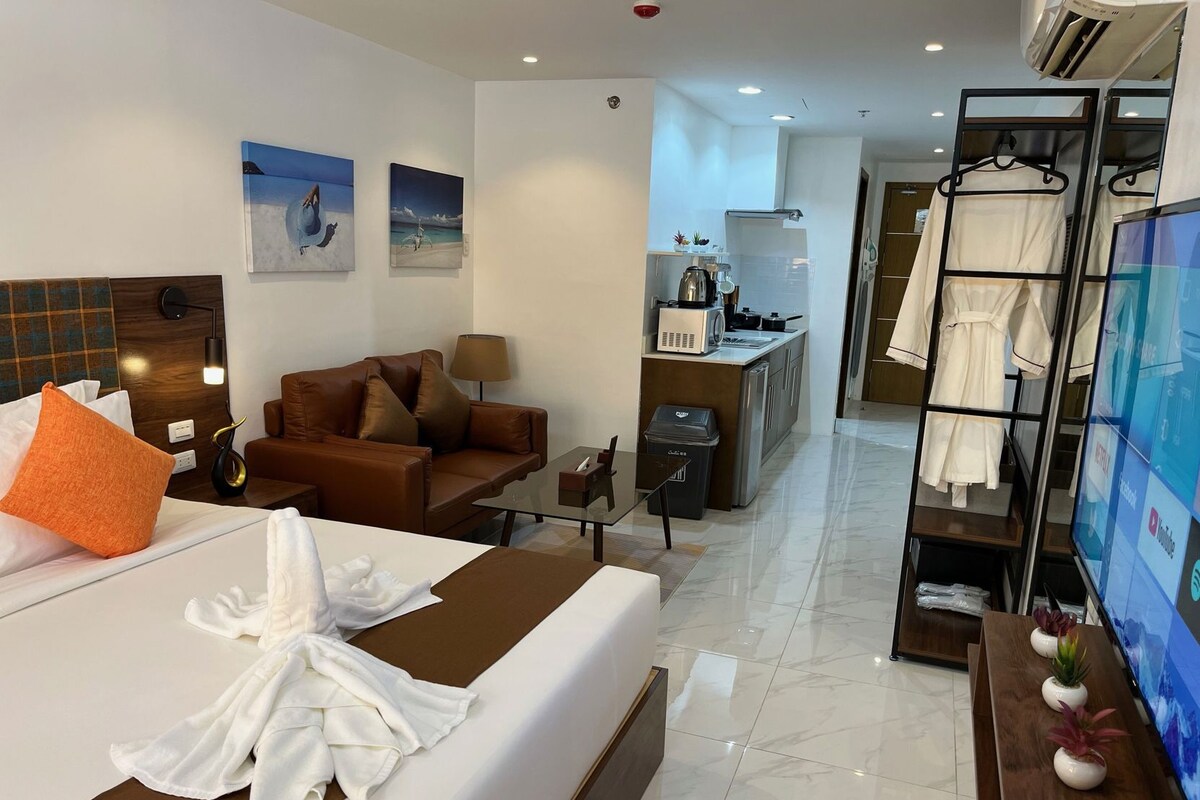 A hotel room with a bed, a sofa, a desk, a TV, and a kitchenette.