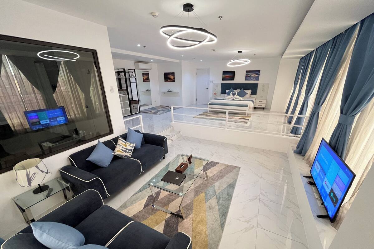 Een moderne woonkamer met een bank, een salontafel en een televisie. Er is een trap die naar een hoger niveau leidt.