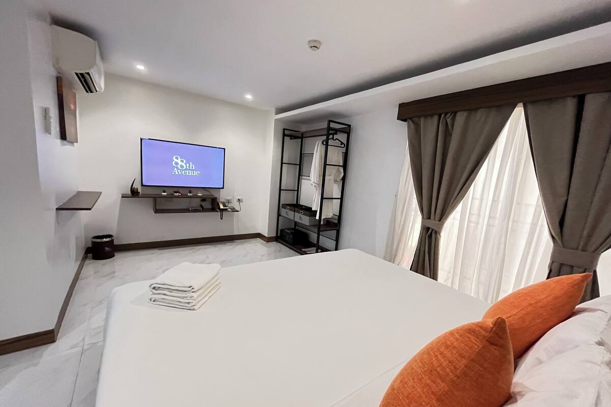 Een moderne hotelkamer met een groot bed, een flatscreen televisie aan de muur, een nachtkastje, een spiegel en een raam met gordijnen.