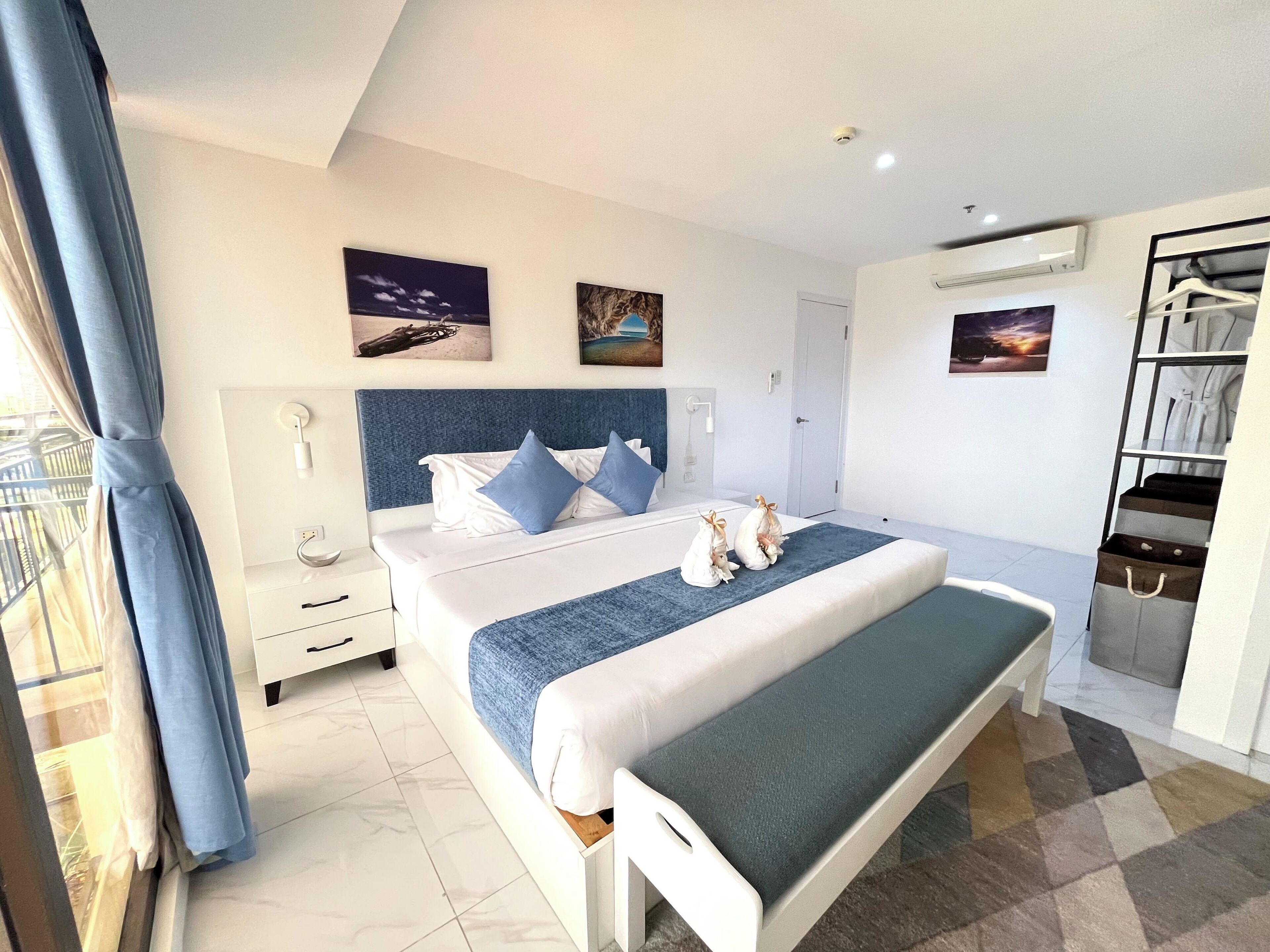 A modern hotel room with a large bed, a bedside table, a wardrobe, and a balcony with curtains.