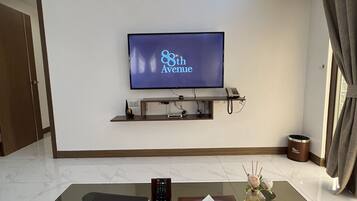 A modern living room with a flat-screen TV mounted on the wall, a glass coffee table, a laptop, a remote control, a tissue box, and a decorative vase.