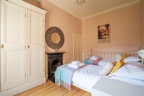 A bedroom with a bed, a fireplace, a wardrobe, and a wall with a framed picture.