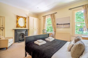 Une chambre avec une cheminée, un lit avec des serviettes, une chaise et une fenêtre avec des rideaux.