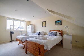 A bedroom with two beds, a desk, a wardrobe, and a window.
