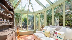 A conservatory with a glass ceiling, a white sofa with decorative pillows, and a wooden cabinet with dishes. - 7 St John's Crescent -  a family break that sleeps 6 guests  in 3 bedrooms (York)