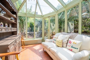 A conservatory with a glass ceiling, a white sofa with decorative pillows, and a wooden cabinet with dishes. - 7 St John's Crescent -  a family break that sleeps 6 guests  in 3 bedrooms (York)