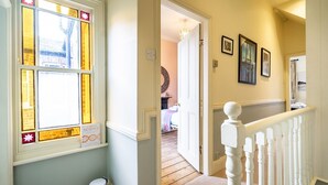 A hallway with a white railing, a door leading to a bedroom, and a window with stained glass. - 7 St John's Crescent -  a family break that sleeps 6 guests  in 3 bedrooms (York)