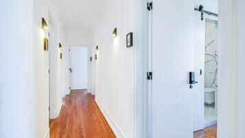 A hallway with wooden flooring, white walls, and wall-mounted lighting fixtures.