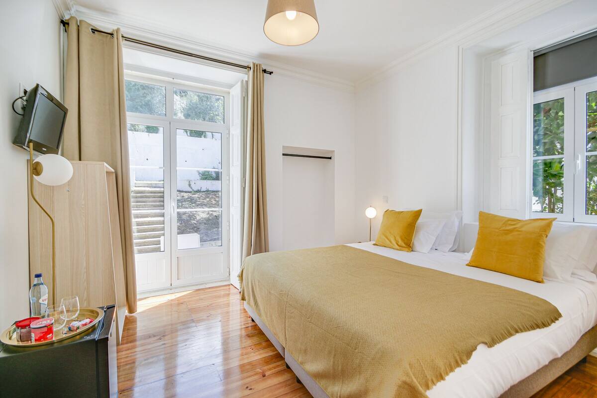 Quarto com uma cama grande, televisão na parede e janela com cortinas.