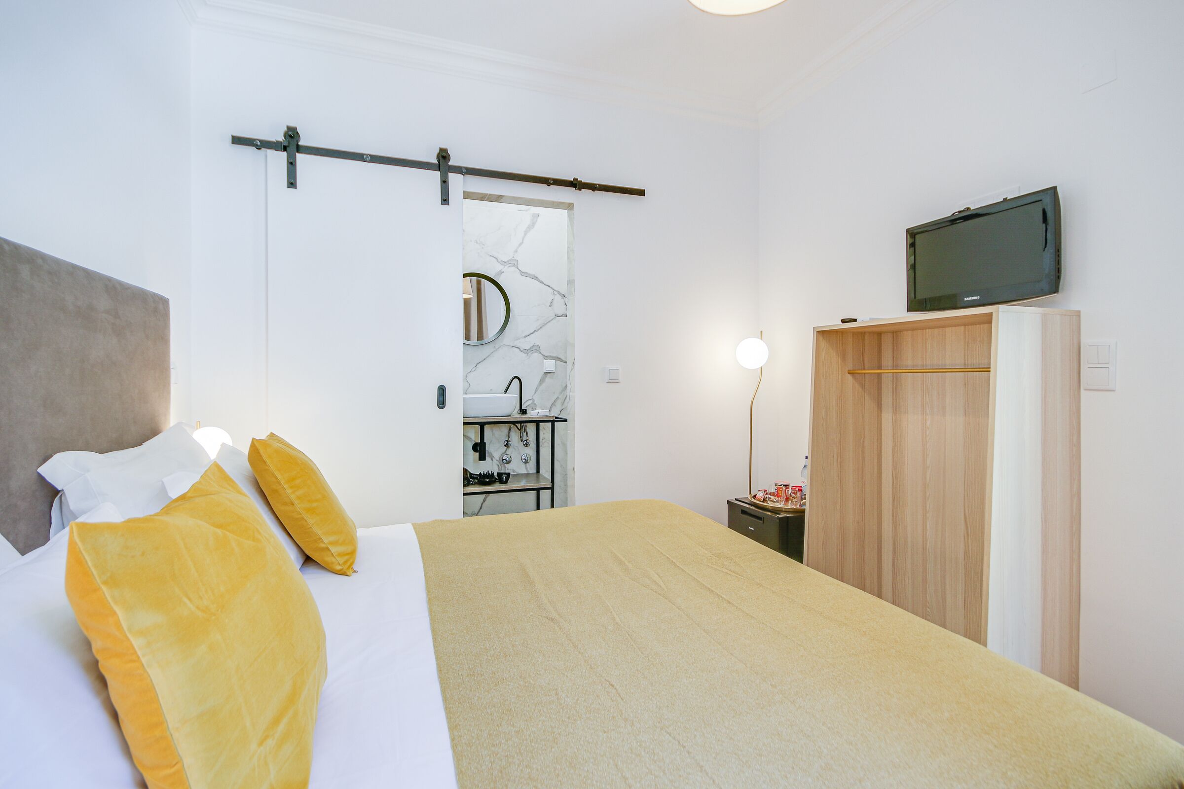 A bedroom with a bed, a bedside table, a mirror, a television, and a wardrobe.