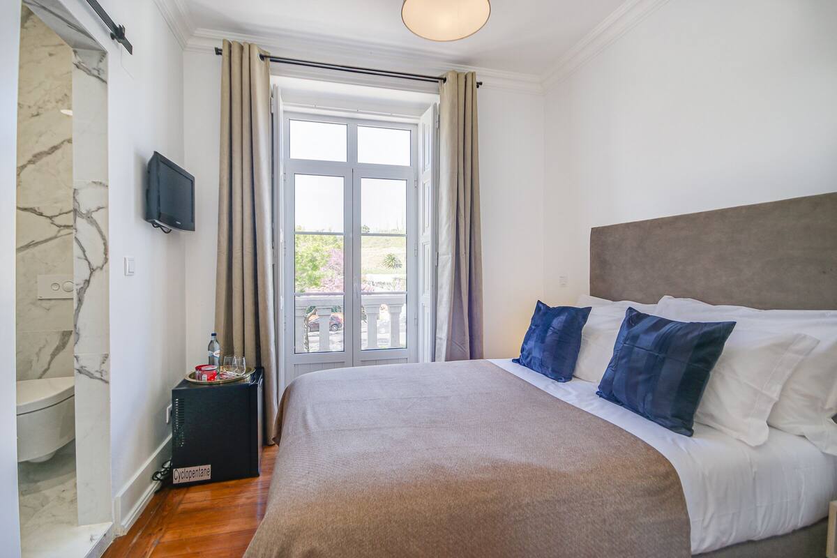 Quarto com cama grande, televisão na parede e vista para o exterior através de uma porta de vidro.